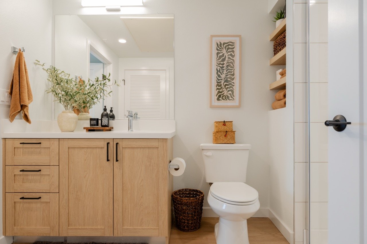 White oak vanity with soft-close drawers beside a tiled shower and open shelving niche