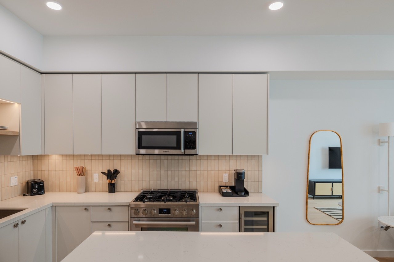 Ceiling-height frameless matte kitchen cabinetry with gas range and integrated wine refrigerator in an apartment unit