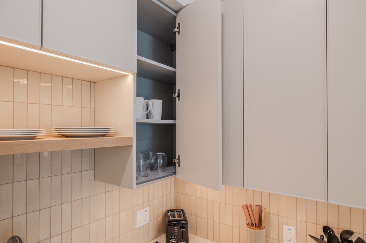 Open frameless upper cabinet showing concealed European hinges, adjustable shelving, and integrated under-cabinet LED lighting