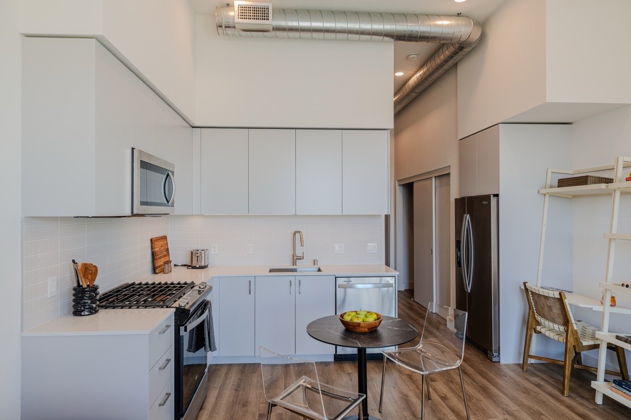 Frameless white European kitchen cabinetry with full-height upper cabinets in an apartment unit