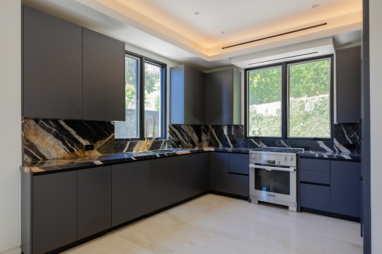 Charcoal matte L-shaped kitchen with a full-height marble backsplash and brass fittings