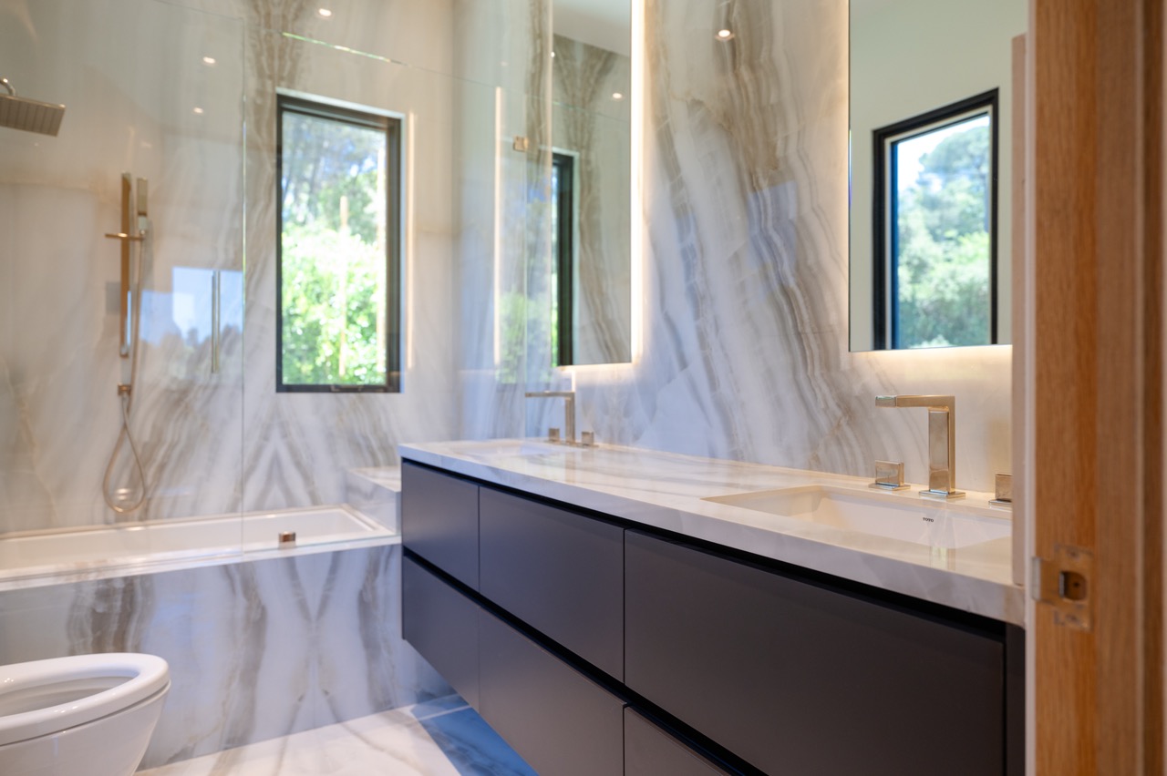 Onyx-clad bathroom with a wall-hung navy double vanity and backlit mirrors