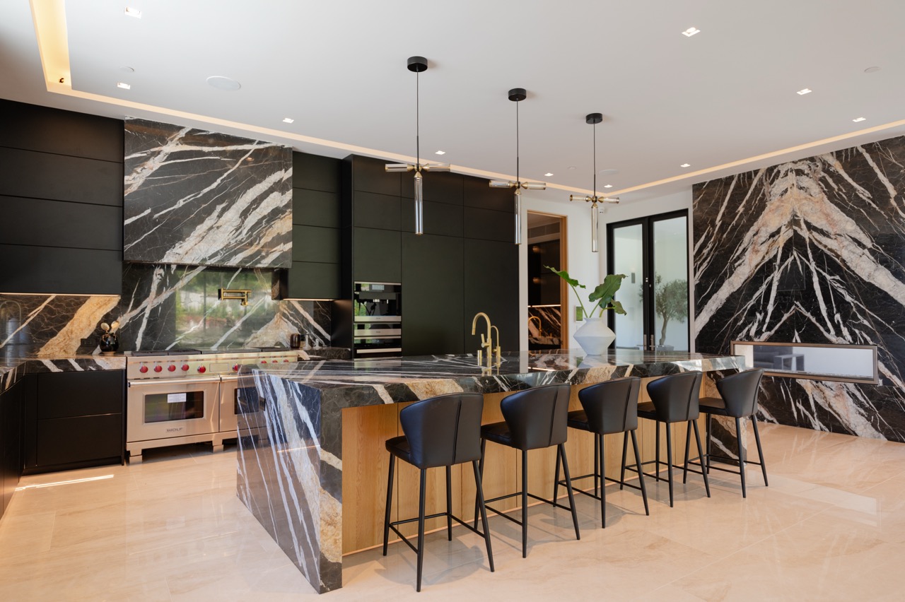 Matte black kitchen with a professional range, marble feature wall, and oak-backed island seating