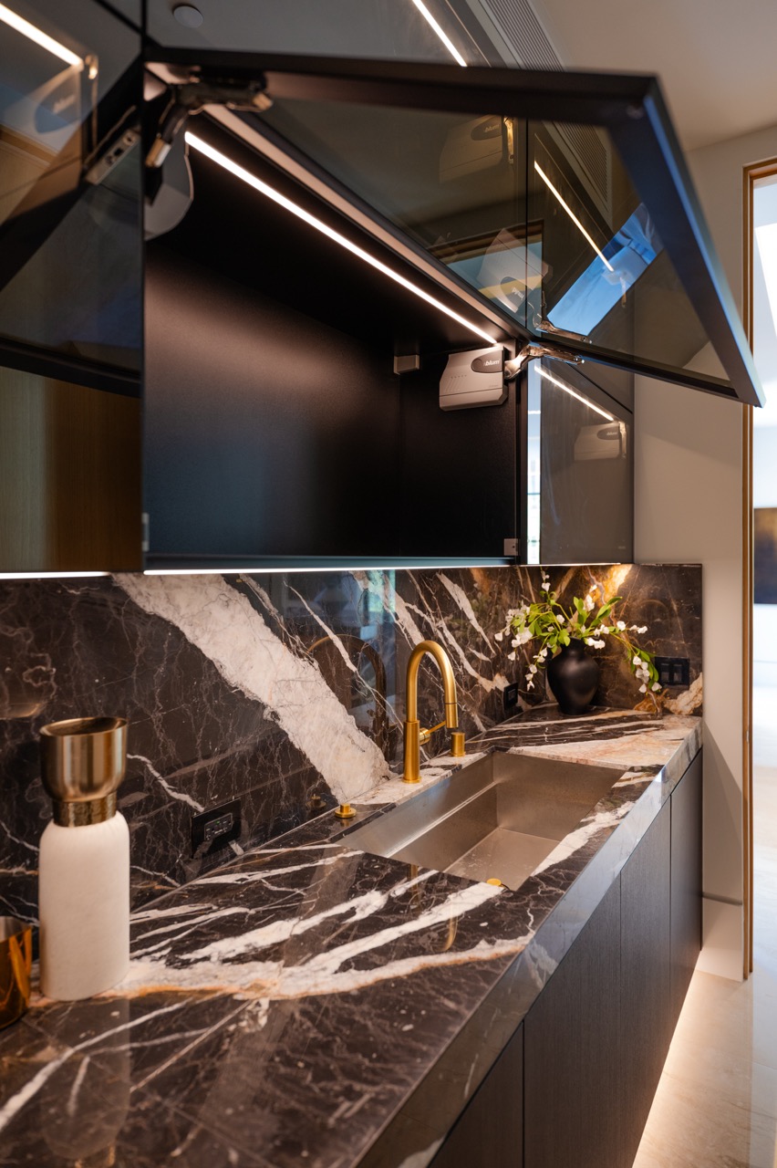 Glass-fronted upper cabinets on lift-up soft-close hardware, with integrated LED and a marble backsplash