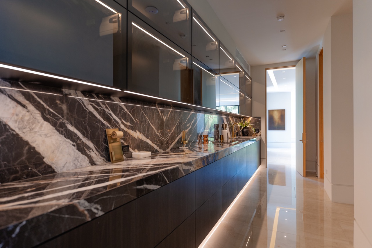 Butler's pantry with glass-fronted upper cabinets, integrated LED lighting, and a marble backsplash
