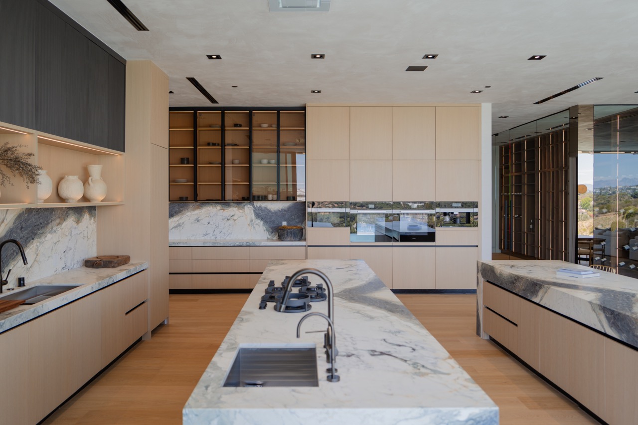 Pale oak kitchen with glass display cabinetry, marble backsplash, and integrated appliance wall