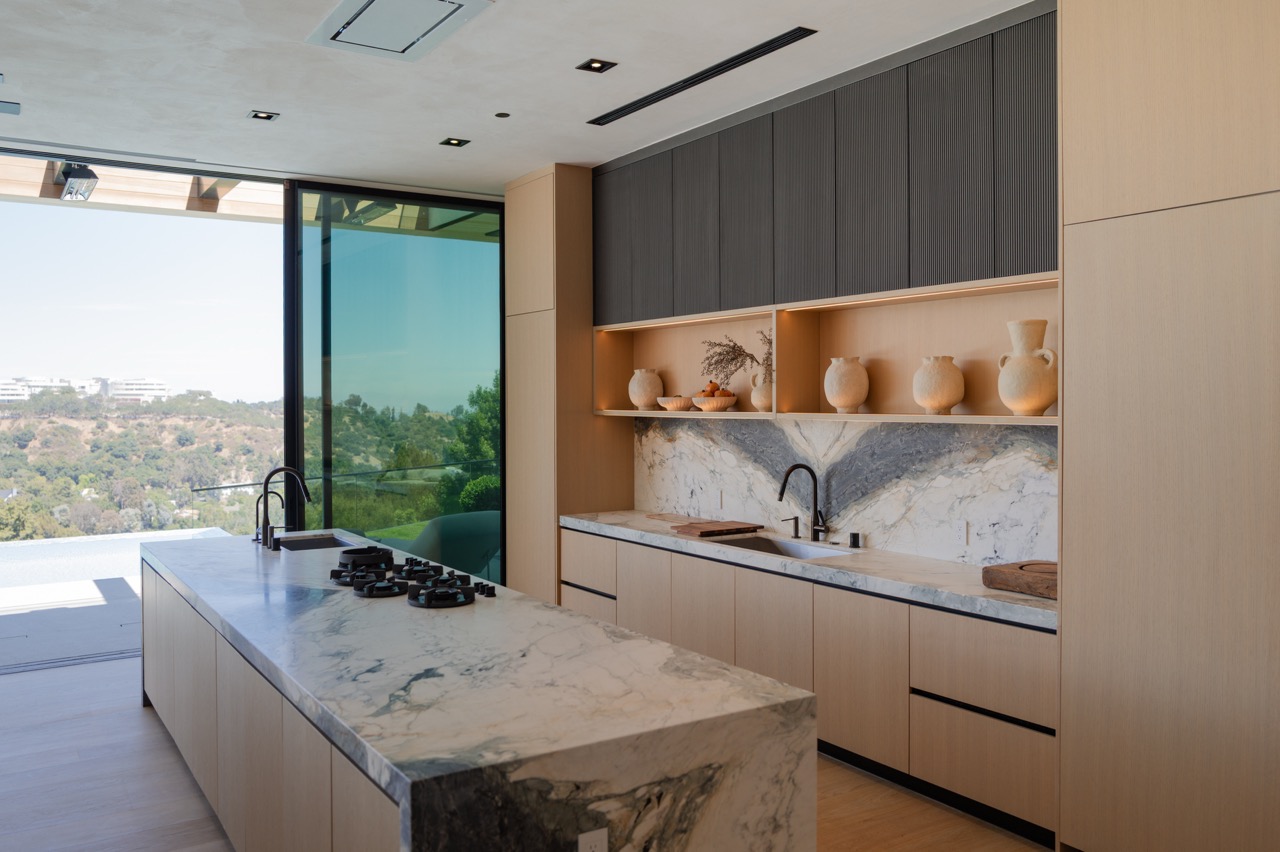 Pale oak kitchen with a marble island cooktop and fluted charcoal uppers, opening to a terrace
