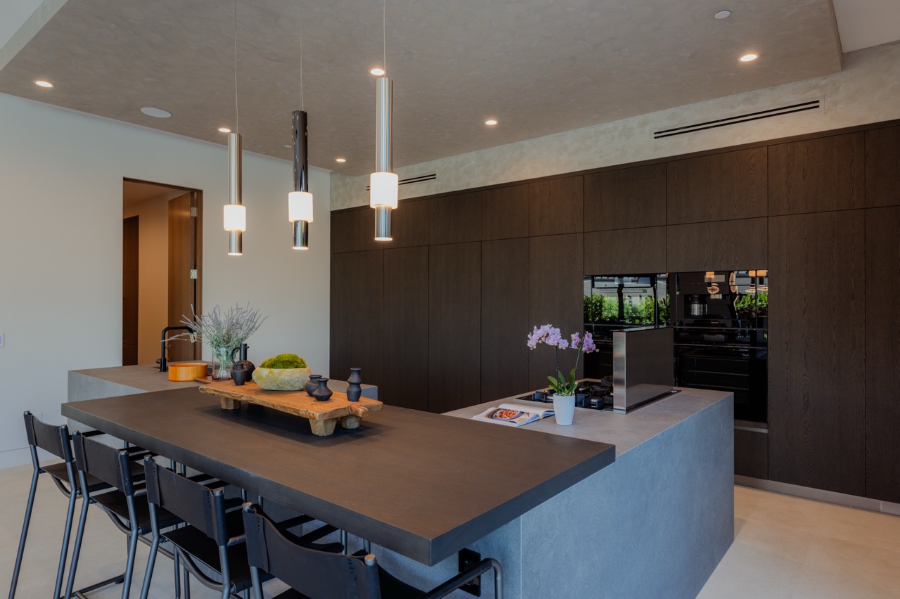 Dark oak kitchen with a stone island, pendant lighting, and a full wall of integrated cabinetry