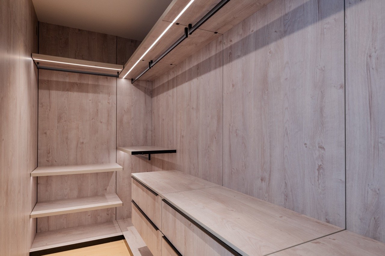 Pale oak walk-in with backlit rails, open shelving and a full run of drawers
