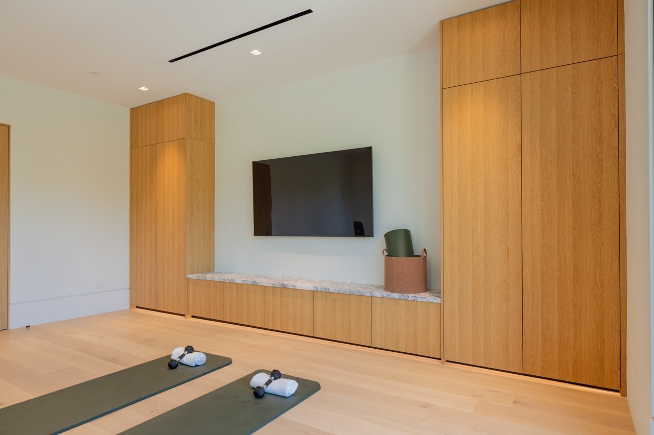 Fitness room storage wall in oak with a stone ledge and concealed cabinetry