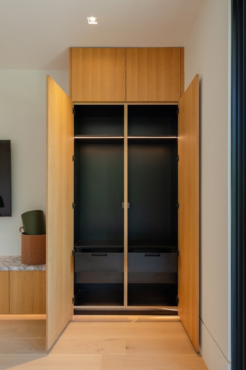 Wardrobe opened to a dark interior with a lit hanging rail and full-extension drawers