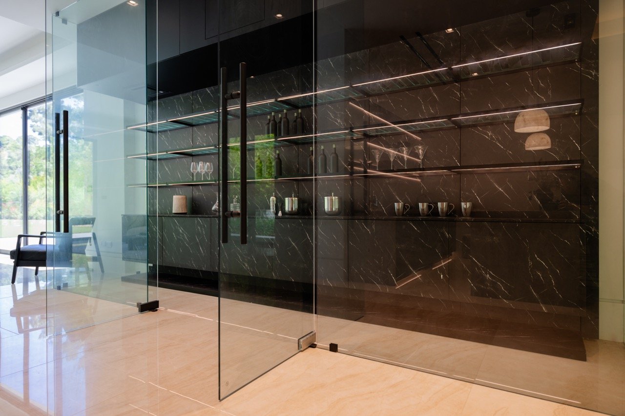 Bar in book-matched marble behind glass, with lit glass shelving