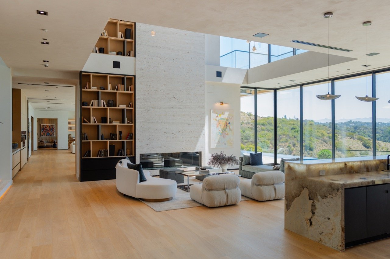 Double-height bookcase tower beside a travertine fireplace