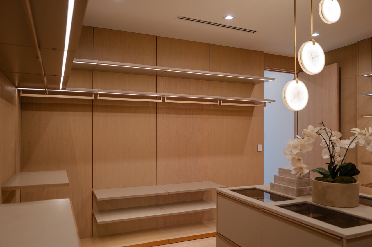 Walk-in closet with a glass-topped island, backlit hanging rails and alabaster pendants